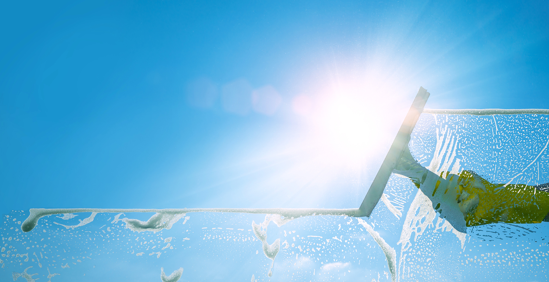 Window cleaner cleaning window with squeegee and wiper on a sunny day with a bright blue sky.